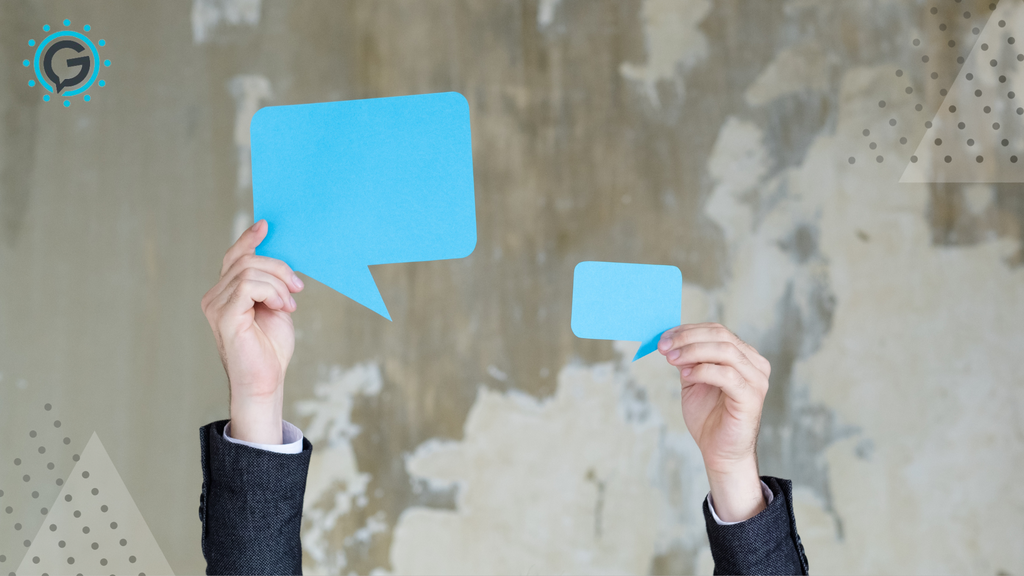 The hands of a man in a suit holding up two blue paper cutouts of speech bubbles, one in each hand. The background is grey.