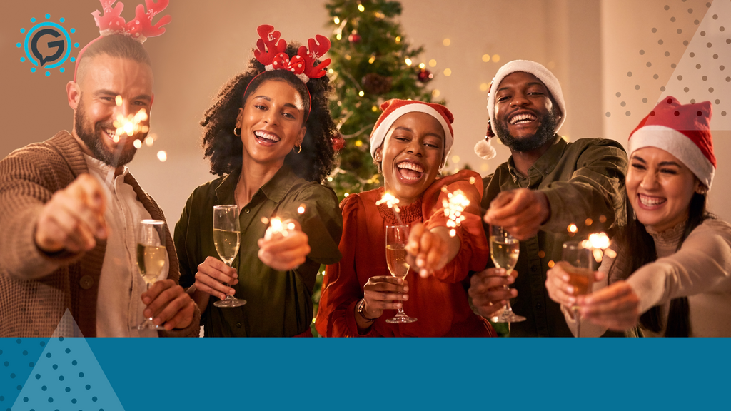 One white man, one white woman, two black women and one lack man raise glasses of champagne and sparklers toward the camera. They are wearing red and white santa hats with a christmas tree in the background.