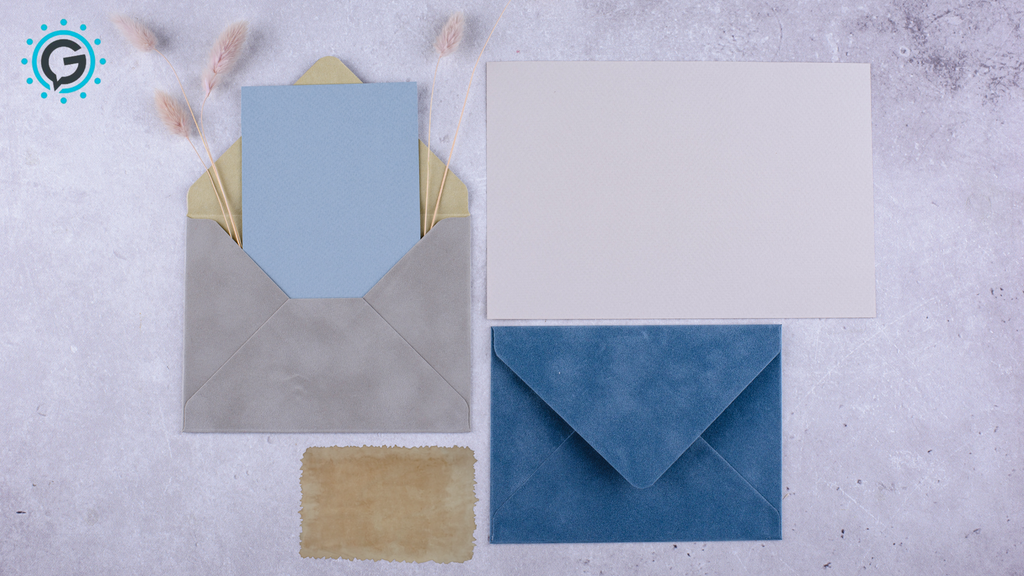 One grey envelope with a blue piece of paper in it, a dark blue envelope, and a white piece of paper all sitting on a light grey surface.