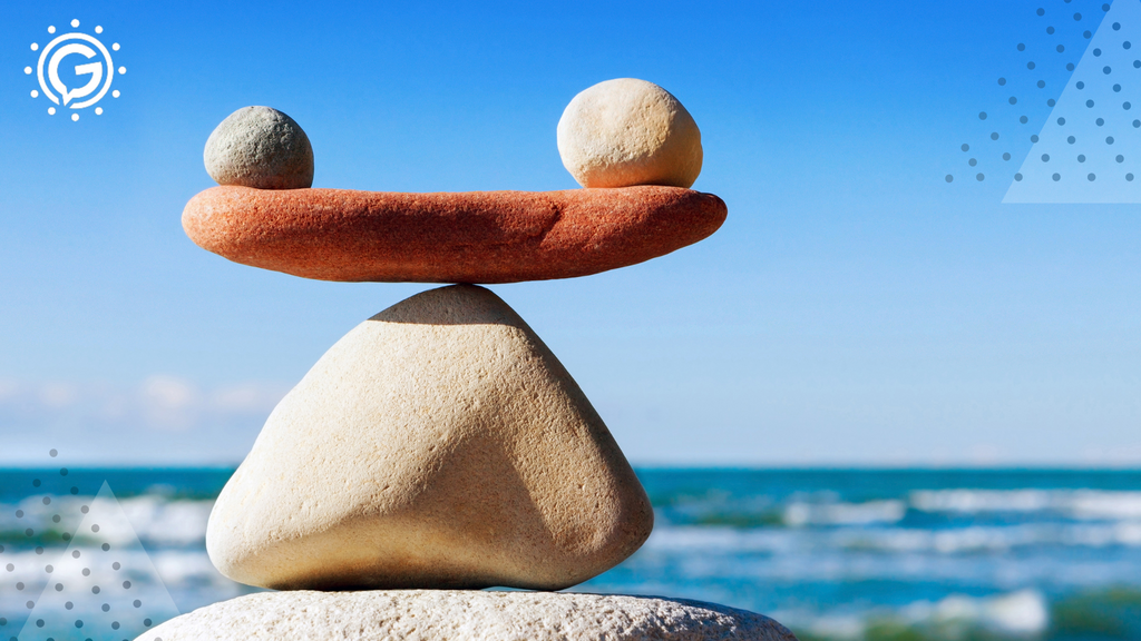 Two small round rocks stacked on top of a small flat rock stacked on top of one triangular rock. Blue sky and the ocean line is in the background.