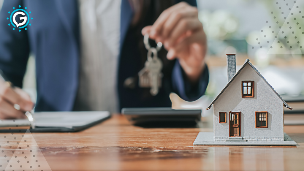 A miniature version of a small house with a man holding house keys in the background.