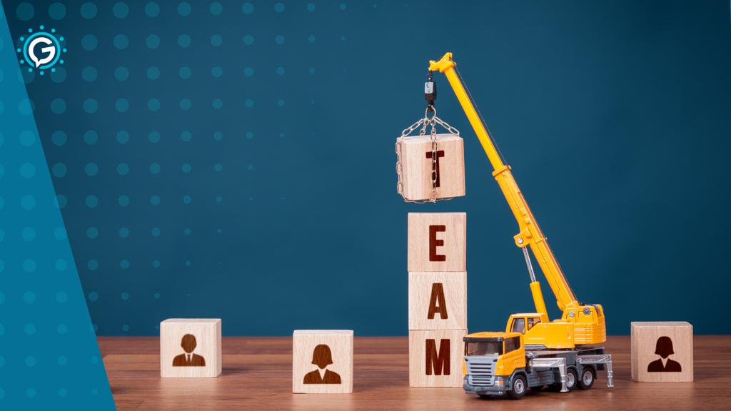 A miniature toy crane placing a block with the letter "T" on it on top of a stack of four blocks spelling the word "team."