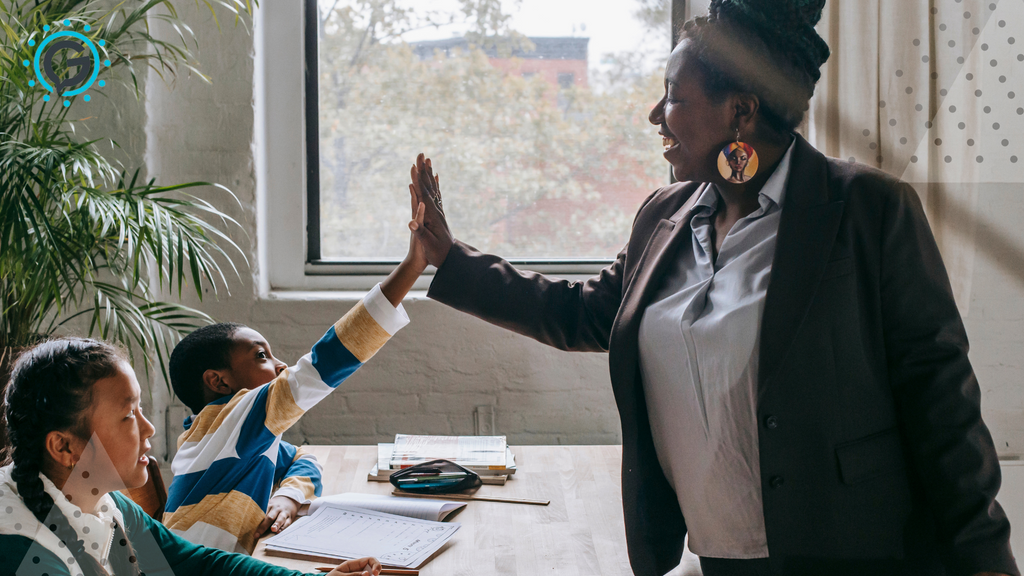 A smiling black woman in a dark grey blazer and white button up shirt giving a high five to a small black boy sitting next to a young black girl.