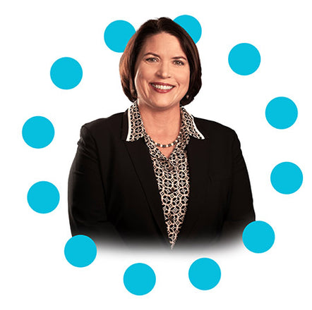 Female caucasian CEO Brenda headshot in a circle of blue dots. Brenda has short brown hair and is wearing a print button up with black blazer.