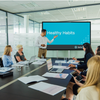 A man introducing the meeting module video on a screen in a conference room of employees.